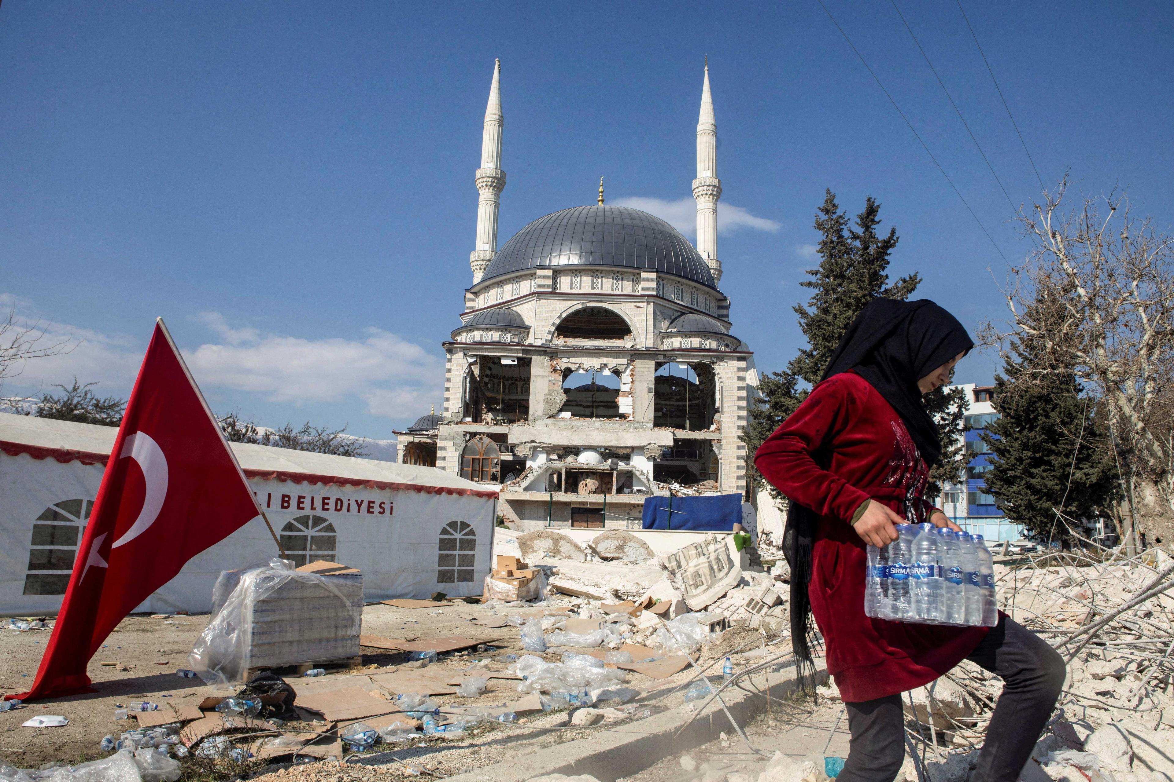 Seorang remaja perempuan mengendong sekotak botol air minuman berdekatan masjid yang musnah teruk akibat gempa bumi dahsyat di Antakya, Turkiye, 16 Februari. Gambar: Reuters