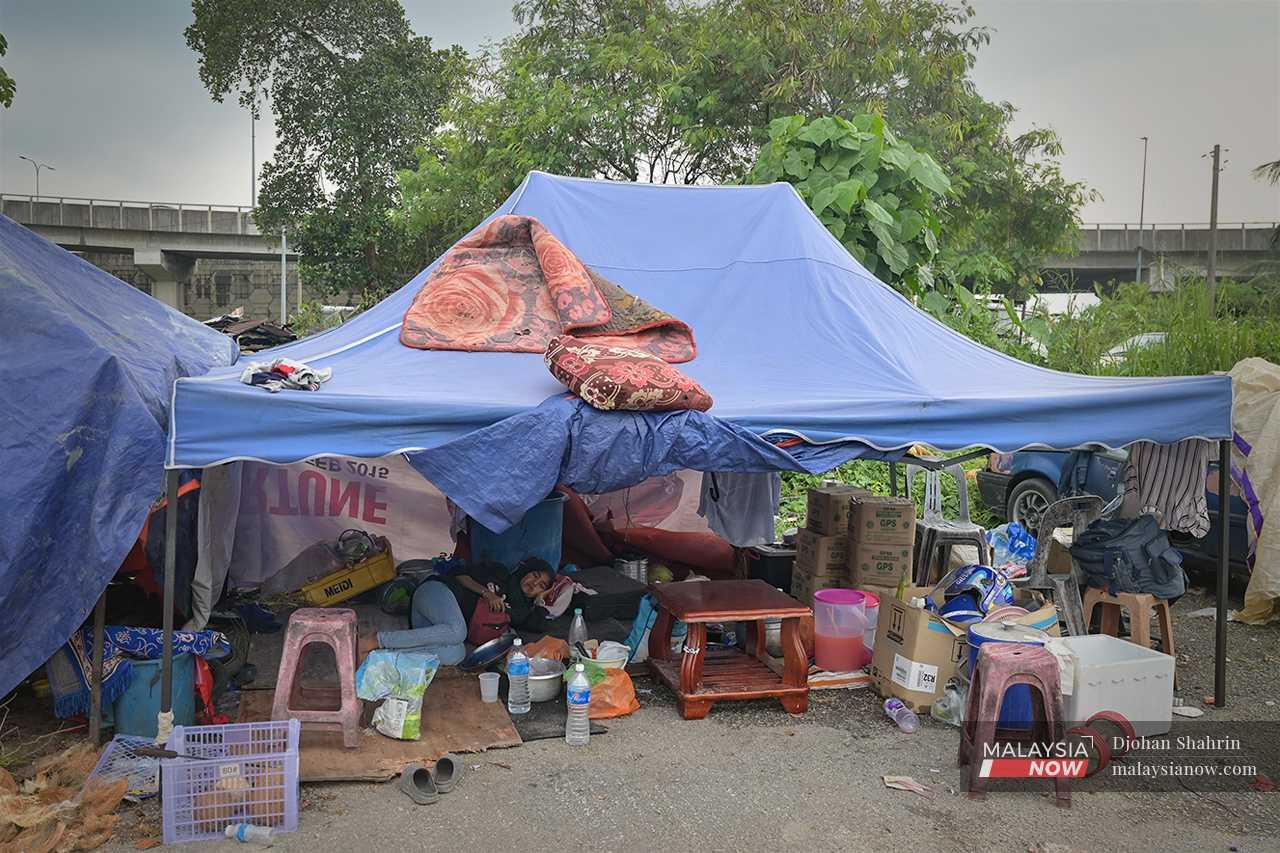 Seorang penduduk berehat di bawah khemah selepas kepenatan mencari barang peribadi mereka.