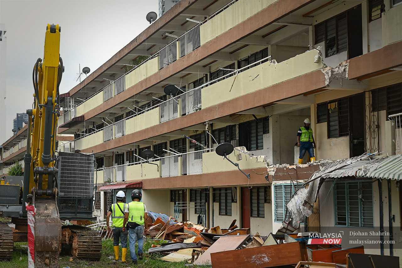 Beberapa pekerja meninjau kawasan yang dirobohkan, di mana kelihatan perabut dan besi bersepah di merata tempat.