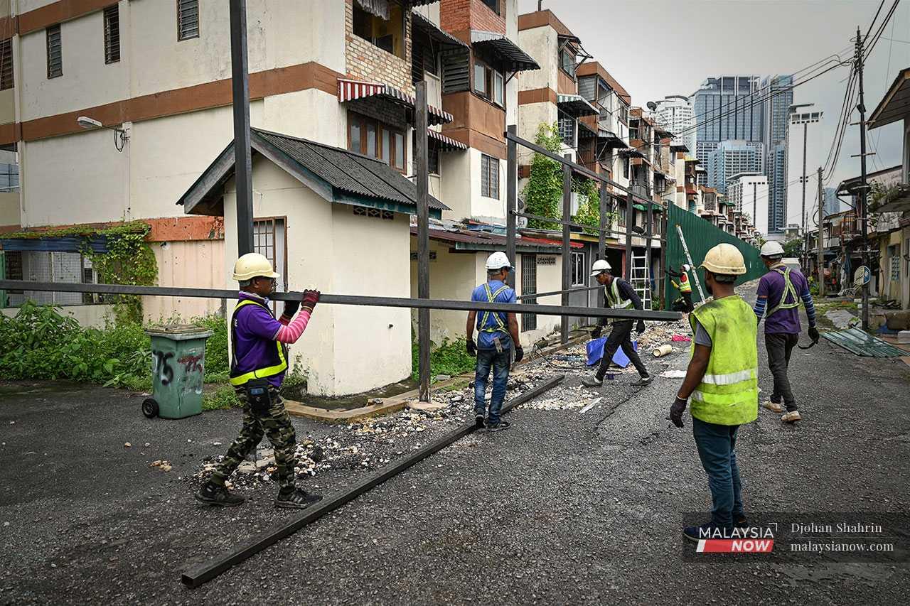 Pekerja membawa besi dan memasang zink biru untuk menutupi kawasan perumahan flat, meneruskan kerja perobohan walaupun dibantah penduduk melalui tindakan mahkamah.