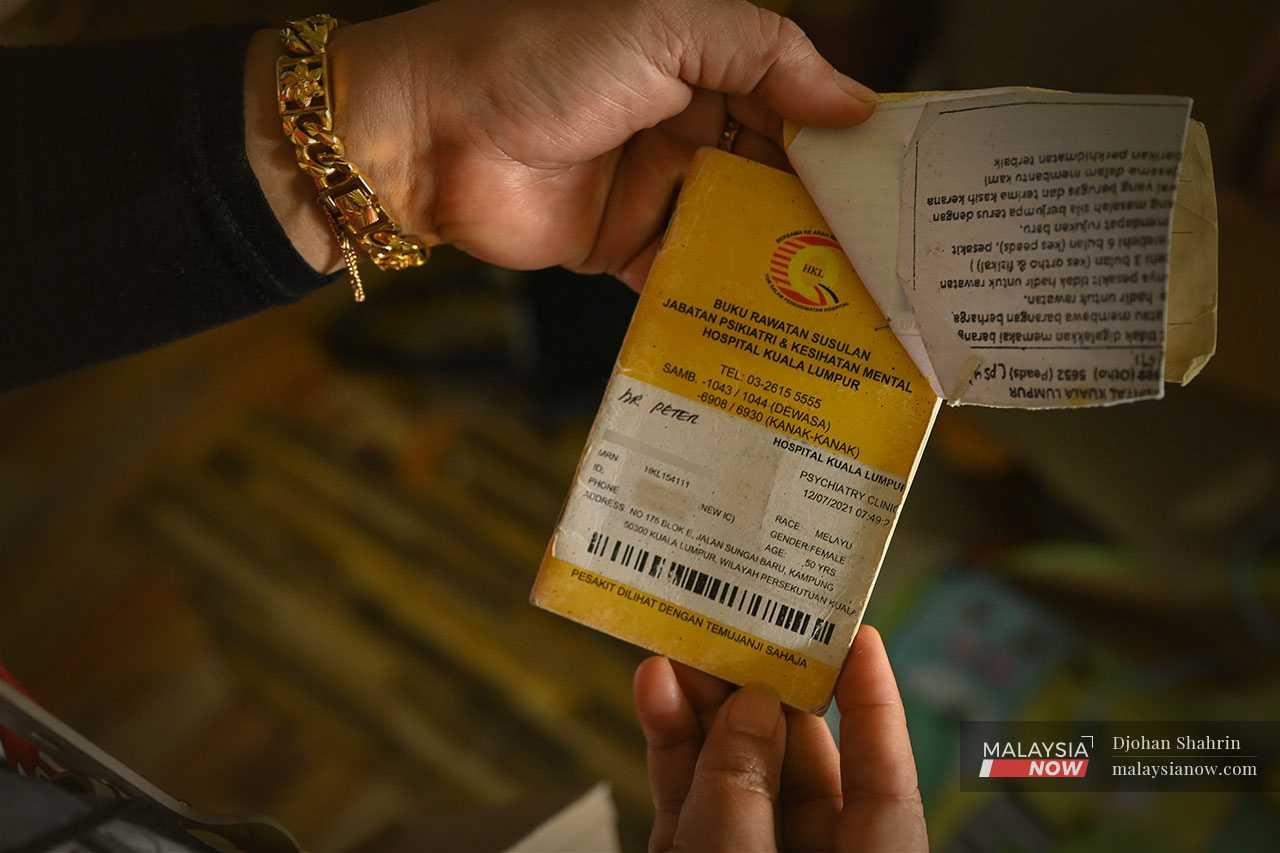 Zura, who has been very stressed about their situation, holds up a booklet from the psychiatry and mental health department at Hospital Kuala Lumpur.