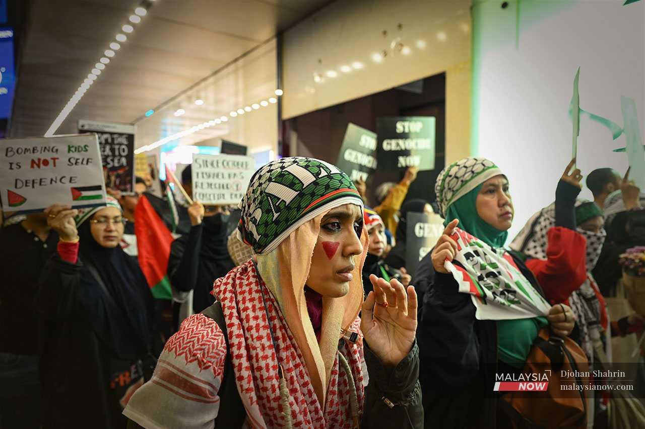 Sekumpulan wanita dengan pelekat muka bertemakan warna bendera Palestin berarak di kaki lima pusat beli belah Lot 10, Bukit Bintang.