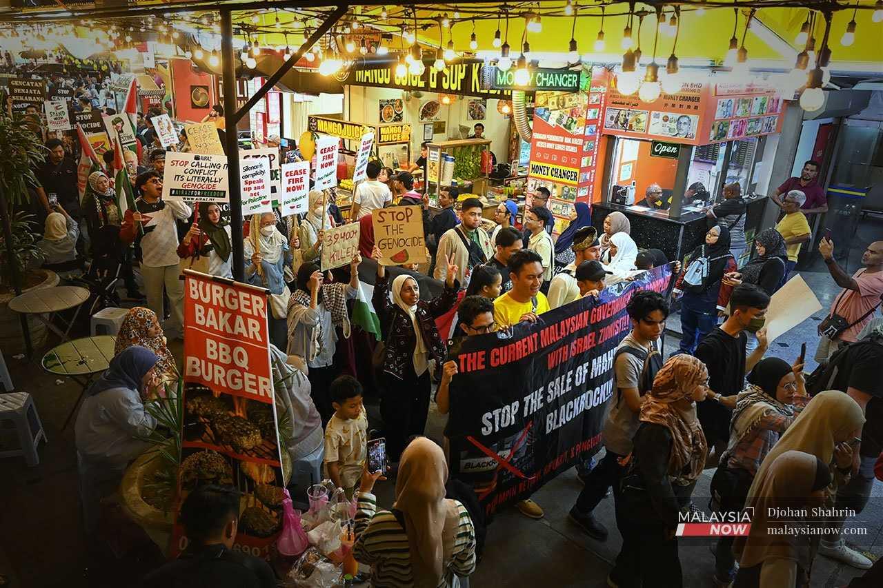 Pro-Palestine protesters march through the busy Saturday night crowd in Bukit Bintang on Aug 3, 2024, calling on the government to cancel its plan to bring in a company owned by BlackRock to manage airports nationwide.