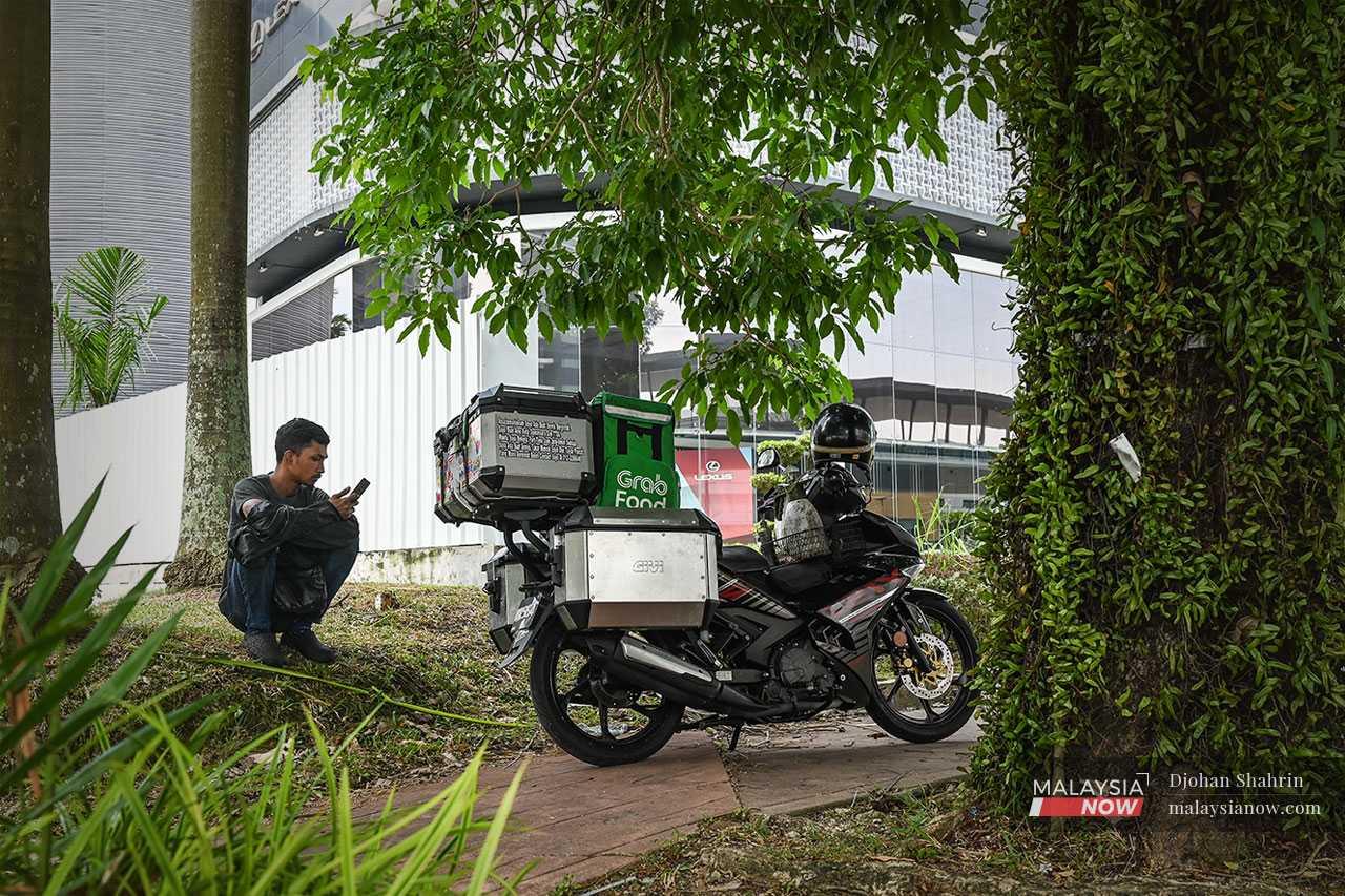 The 29-year-old father of two has three jobs: he is an e-hailing rider, a motorbike mechanic and runs an online shop for spare parts. Here he waits for orders via his e-hailing app on his phone.