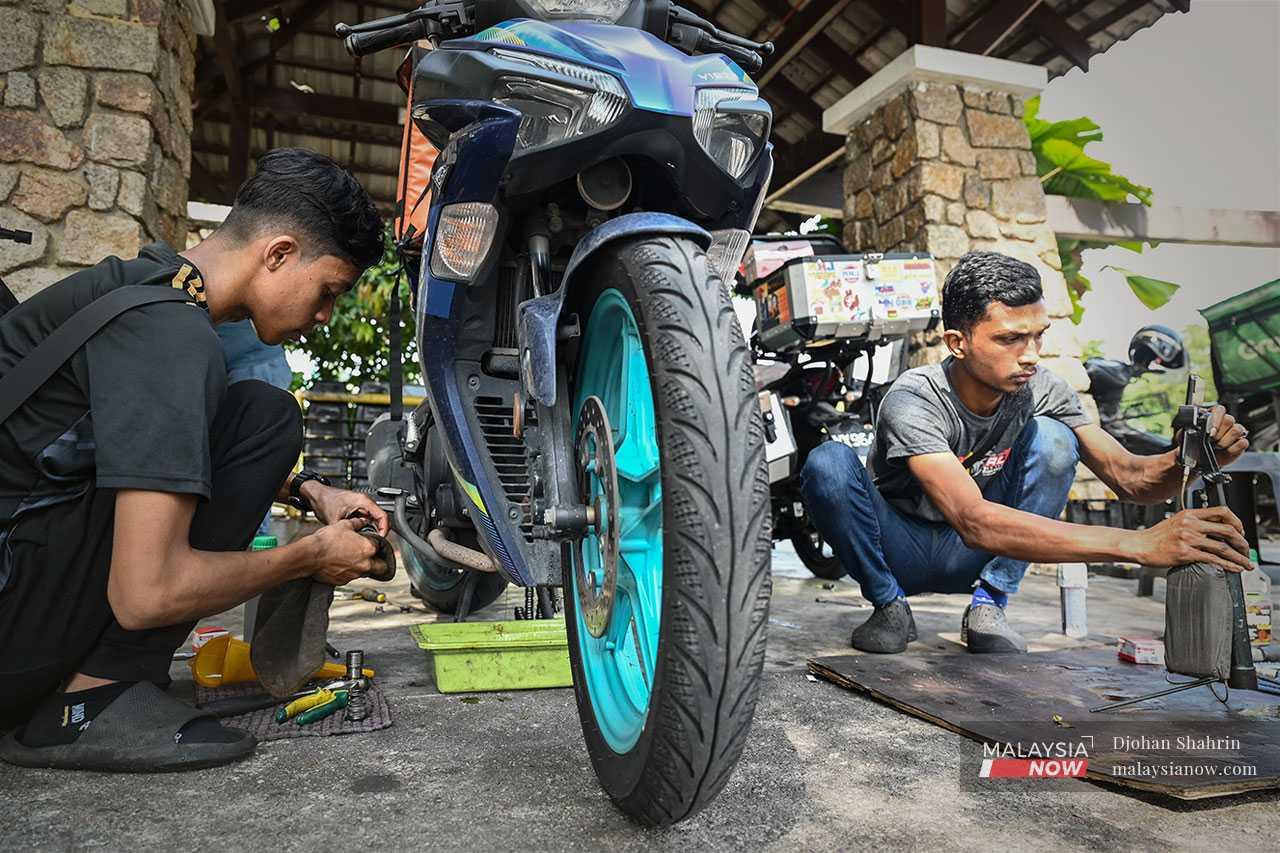 Yusof's assistant Ahmad Haikal carries out repair work on a motorbike.