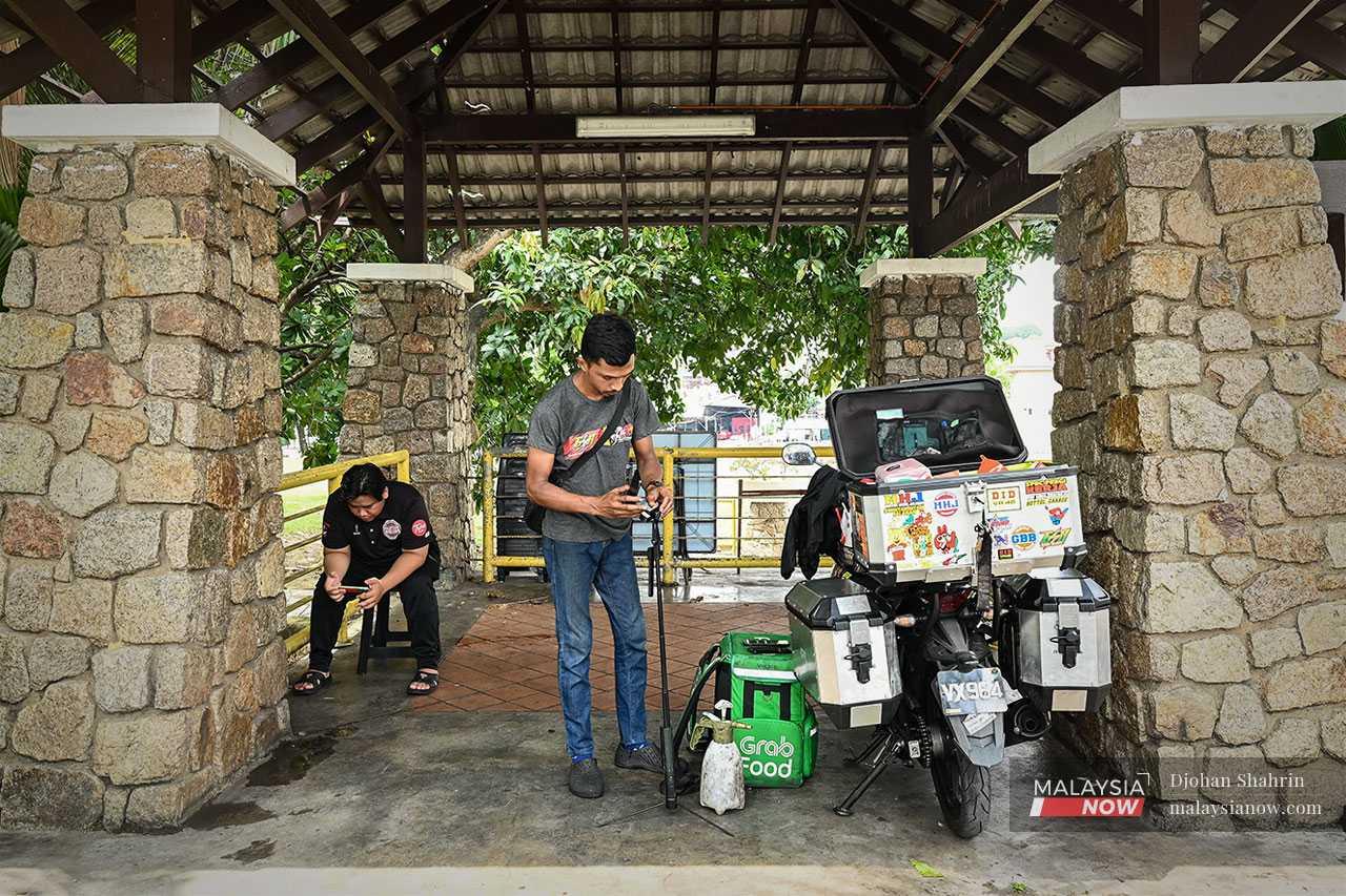 Yusof uses social media platforms such as TikTok to publicise his services. Here he prepares his video while a customer waits for his motorbike to be serviced.