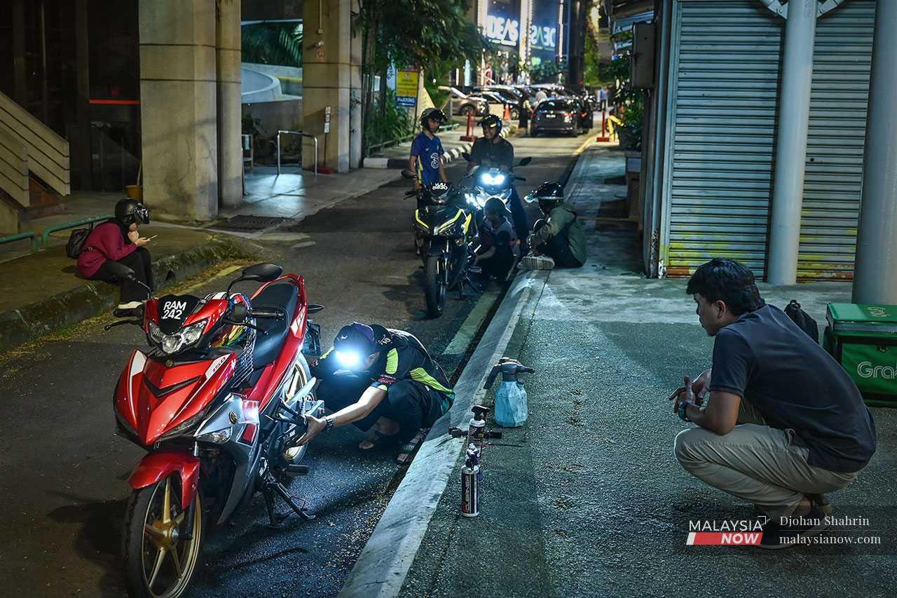 Seorang pemilik motosikal menunggu pasukan Minyak Hitam Jalanan melakukan servis di tepi jalan.