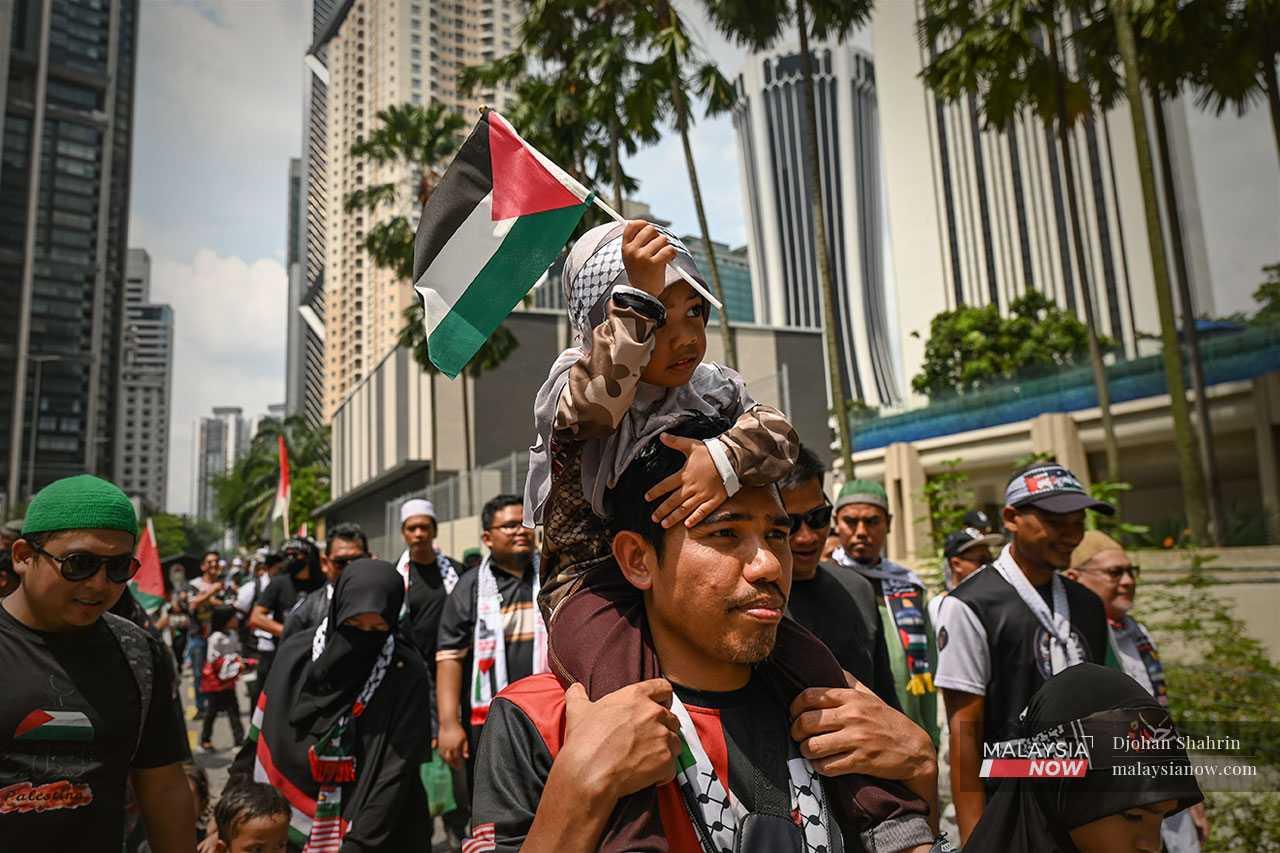 A child on his father's shoulders waves the Palestinian flag as tens of thousands commemorate one year of genocide in Gaza.