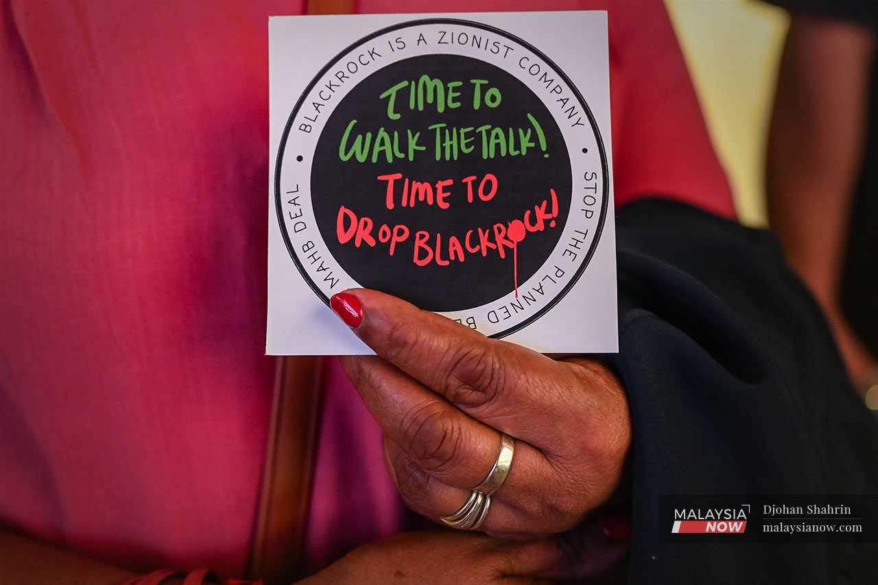 An activist holds a sign calling for an end to the involvement of BlackRock in Malaysia Airports Holdings shares.