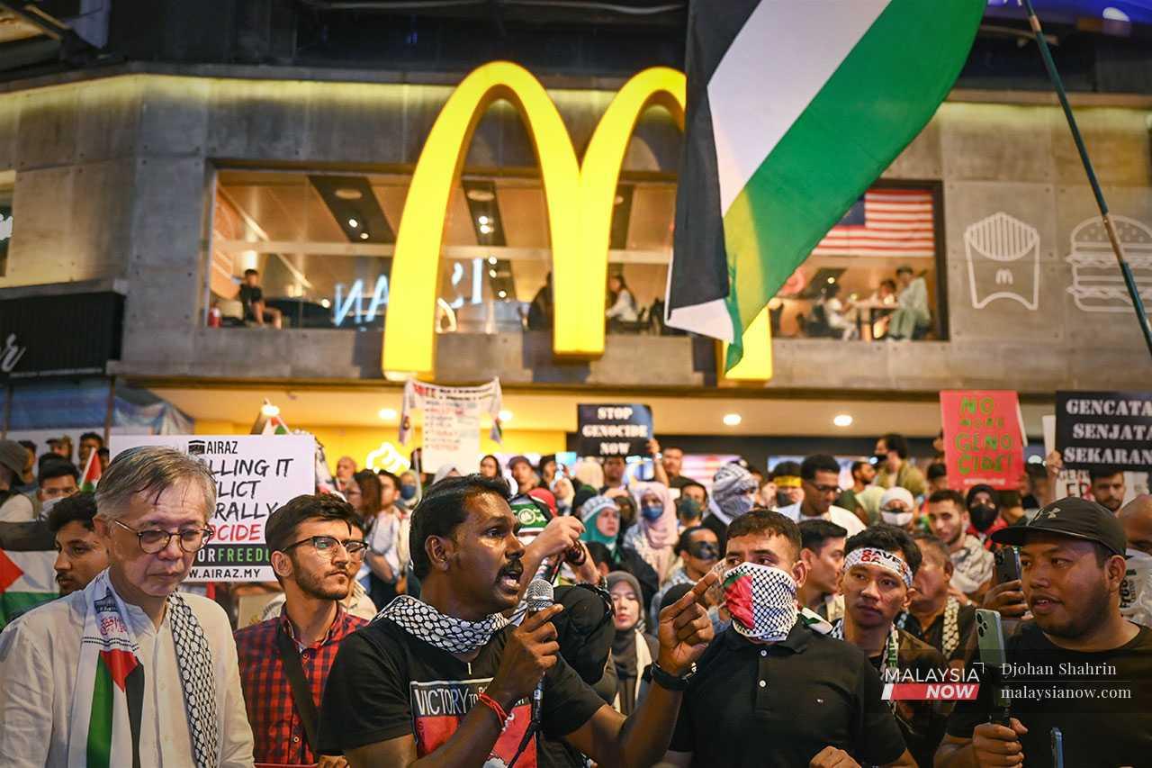 Mythreyar menggunakan pembesar suara di luar sebuah restoran McDonald's di Kuala Lumpur, disertai Tian Chua, jurucakap Sekretariat Solidariti Palestin.