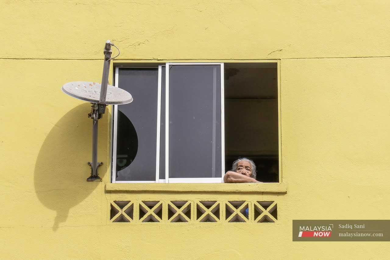 An elderly woman gazes out of the window of her home at a low-cost housing unit in Kuala Lumpur. While advanced age is a factor in the onset of Parkinson's disease, other factors can also contribute such as environmental pollution and genetics.