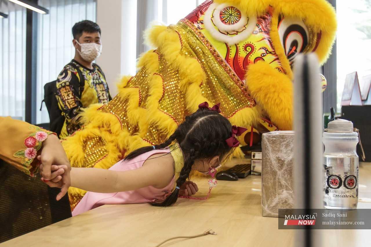A young girl peeks at a dancer during a lion dance performance at an office in Klang, ahead of Chinese New Year, Jan 20.