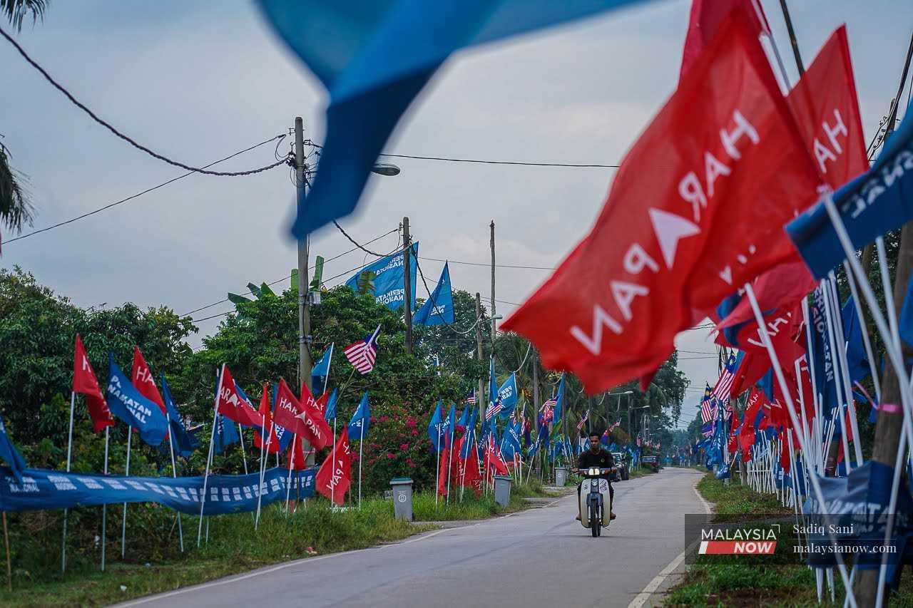 A motorcyclist passes the flags of Perikatan Nasional and Pakatan Harapan in Simpang Jeram, ahead of the by-election on Sept 9.